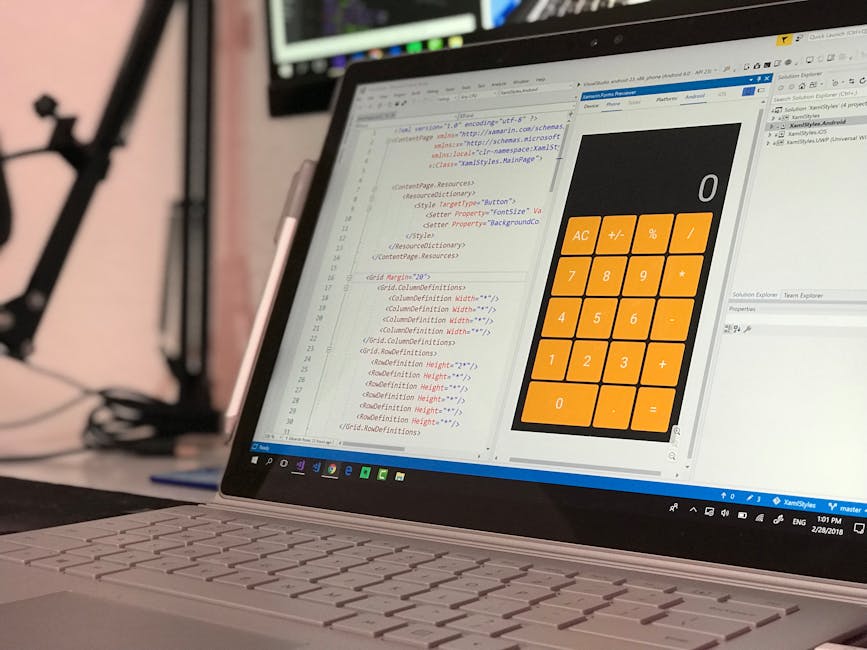 Close-up of a laptop on a desk displaying a code editor with HTML and CSS code on the left side and a colorful calculator interface on the right side. The keyboard is visible at the bottom, and the ba